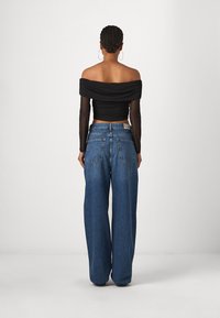 Czarny top bez ramiączek z długimi, przezroczystymi rękawami, zestawiony z niebieskimi dżinsami z wysokim stanem i szerokimi nogawkami. Prosty fason, minimalne detale.