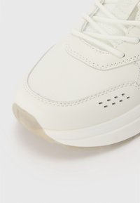 Weiße Leder-Sneaker mit glatter Textur, rundem Zehenbereich, kontrastierenden Nähten und subtilen Perforationen an der Seite. Leichte Sohle.