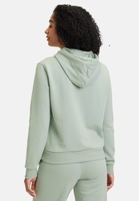 Sudadera verde menta con un bolsillo frontal, puños y dobladillo acanalados, y capucha con cordón. Textura suave y lisa y corte relajado.