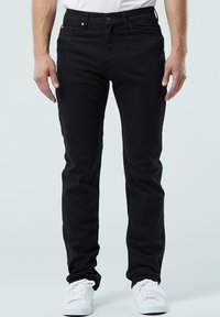 Schwarze Denim-Hosen im Slim-Fit, mit fünf Taschen und Metallknopfverschluss. Getragen mit einem weißen T-Shirt und weißen Sneakern.