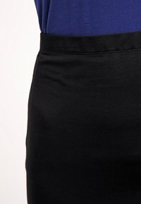 Czarny elastyczny pas spódnicy o gładkiej fakturze, przymocowany do królewsko niebieskiej góry. Widoczne detale szwów na pasie.