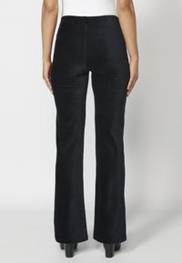 Zwarte corduroy flared broek met een hoge taille, met een soepele textuur en subtiele stiksels, bekeken vanuit de achterkant.