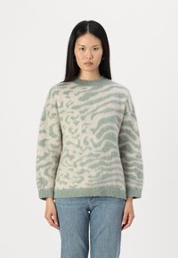 Maglione leggero e oversize in verde pallido e crema con una texture morbida e pelosa, caratterizzato da un motivo a onde. Collo a giro e dettagli con orlo a costine.