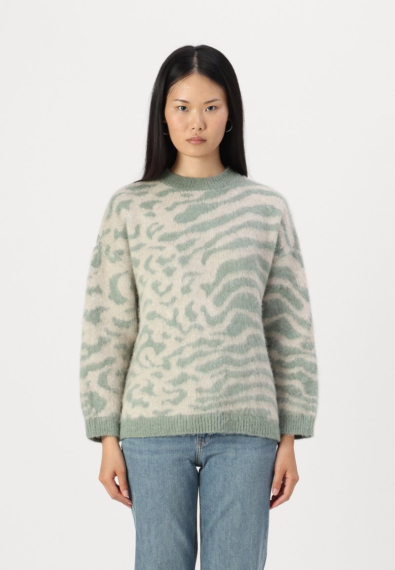 Maglione leggero e oversize in verde pallido e crema con una texture morbida e pelosa, caratterizzato da un motivo a onde. Collo a giro e dettagli con orlo a costine.