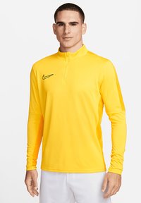 Maglietta sportiva gialla a maniche lunghe con collo a mezza zip. Presenta un logo Nike nero sul petto sinistro. Tessuto leggero e morbido.
