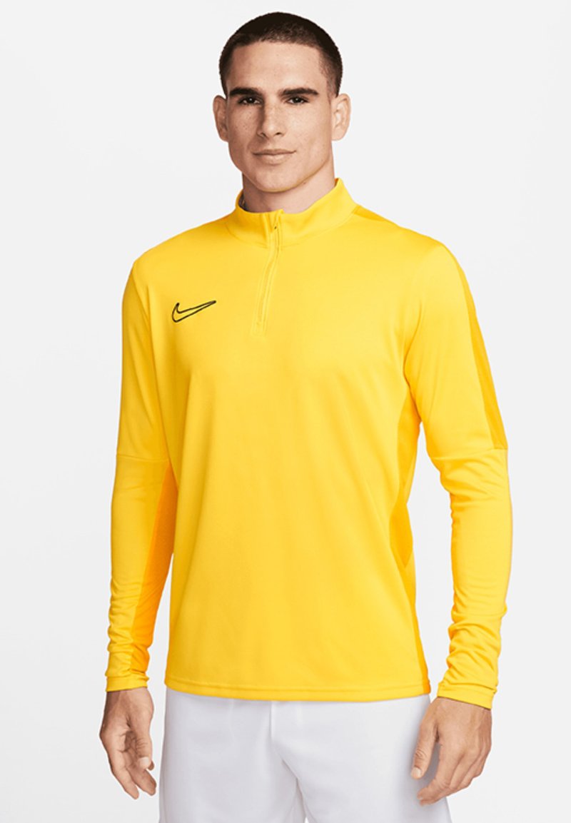 Maglietta sportiva gialla a maniche lunghe con collo a mezza zip. Presenta un logo Nike nero sul petto sinistro. Tessuto leggero e morbido.