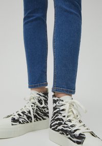 Černobílé vysoké tenisky se zigzagovým vzorem, gumovou podešví a bílými tkaničkami. Nosené s modrými slim-fit džíny.