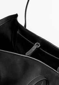 Intérieur d'un sac tote en cuir noir présentant une texture lisse, une petite poche avec une bande, et des coutures discrètes le long des bords.