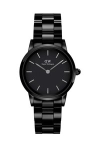 Must mustaühega kell ümmarguse korpuse ja sobiva metallist rihmaga. Kell face'il on lihtsad hõbedased tunni markerid ja käed koos "Daniel Wellington" logo.