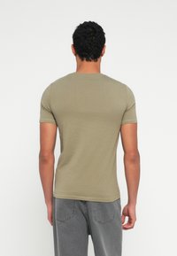 Λαδί κοντομάνικο μπλουζάκι από απαλό ύφασμα με στρογγυλή λαιμόκοψη. Η πίσω όψη δείχνει εφαρμοστή γραμμή και ελάχιστες ραφές.