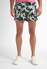 Costume da bagno a fantasia floreale con foglie verdi e fiori bianchi su sfondo blu navy, con vestibilità rilassata e vita standard.