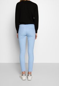 Ljust blå skinny jeans med en slät textur, bakfickor och ankellång fåll. Kombinerat med en svart topp och vita sneakers.