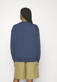 Sudadera azul marino con cuello redondo y puños de canalé, combinada con pantalones cortos caqui con bolsillos laterales. Textura suave y diseño casual.