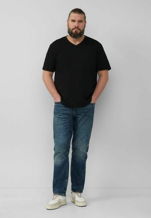 Black short-sleeve V-neck t-shirt, paired with blue straight-leg jeans and beige sneakers, standing against a light gray background.
