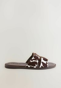 Kossprintade slide-sandaler med en överdel i brun konstläder, breda remmar och en platt, bruntexturerad sula.