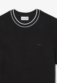 Maglietta in cotone nera con colletto rotondo, caratterizzata da una doppia striscia bianca e un piccolo logo Lacoste nero sul petto. Design a vestibilità regolare.