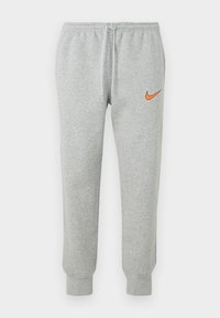 Pelēkas sporta bikses, izgatavotas no kokvilnas maisījuma auduma, ar oranžu Nike logo uz kreisā augšstilba, elastīgu jostasvietu un piegrieztiem potīšu galiem.