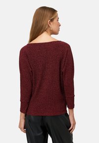 Haut bordeaux scintillant à manches trois-quarts, avec un large décolleté et une coupe ample. Tissu texturé avec une finition douce et brillante.