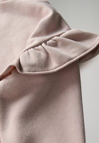 Manga de prenda de algodón color rosa claro con un acento con volantes cerca del hombro, con una textura suave y un ajuste relajado.