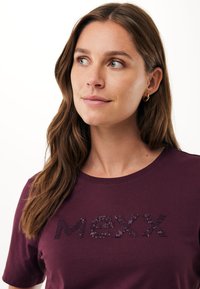 Bordowa koszulka z okrągłym dekoltem, ozdobiona napisem "MEXX" z teksturowanych cekinów. Wykonana z miękkiego materiału, z krótkimi rękawami. Prosty design o gładkim wykończeniu.
