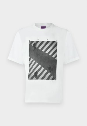 Weißes T-Shirt mit schwarz-weißem Fotodruck von drei Personen, die einen gestreiften Zebrastreifen überqueren, mit dem Schriftzug "HUGO" über dem Bild.