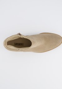 Bota tobillo beige perforada con un acabado suave, cremallera lateral y punta redondeada. Diseño con fuelle para facilitar su uso.