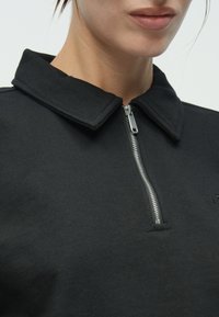 Μαύρο φούτερ με ψηλό γιακά και φερμουάρ μπροστά. Διαθέτει απαλό ύφασμα, λεία υφή και ασημένιο φερμουάρ ως ξεχωριστή λεπτομέρεια.