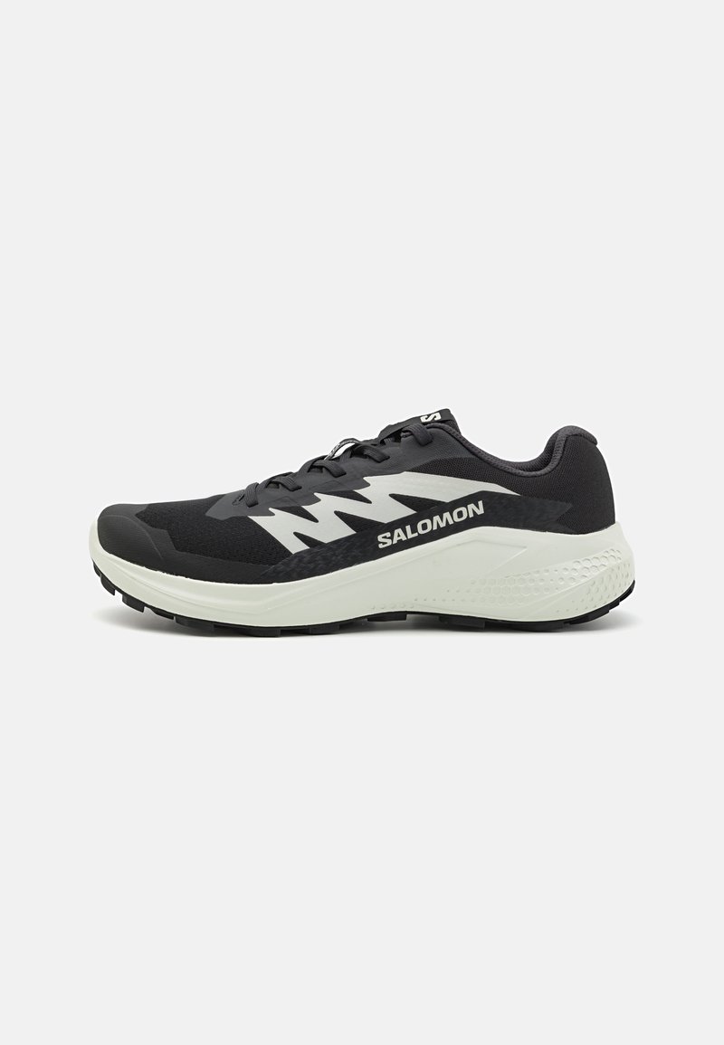 Shoe desportivo preto com um superior de tecido respirável, detalhes em branco e cinza, sola acolchoada e piso texturizado para aderência.