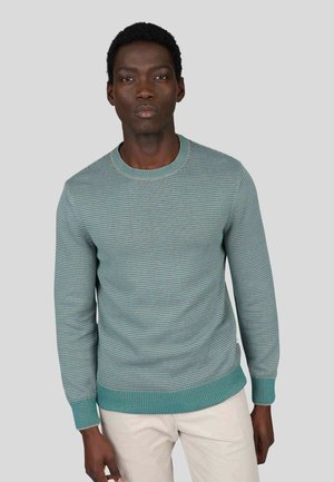 Pull en tricot bleu-vert clair avec un col rond côtelé, un motif uni et des poignets texturés contrastants. Assorti à un pantalon de couleur crème.