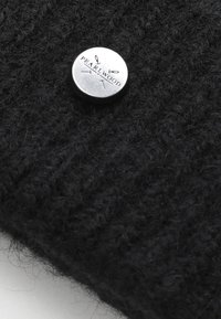 Černá pletená vlněná látka s texturovaným povrchem, se zaobleným stříbrným knoflíkem s reliéfem "PEARLWOOD" a detaily šipky.