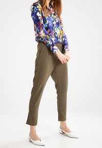 Blommig blus med blå bakgrund och flerfärgade blommor; olivgrön taperad byxor; vita spetsiga ballerinas med sidoklipp.