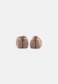 Brown fuzzy slippers with a soft, textured exterior, rounded shape, and a contrasting brown label at the back. Simple and comfortable design.