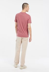 Bordová tričko s krátkym rukávom a okrúhlym výstrihom, skombinované so svetlooranžovými cargo nohavicami. Celý outfit dopĺňajú neutrálne tenisky.