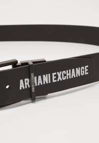 Cintura in pelle nera con fibbia in metallo color argento. Presenta il logo "ARMANI EXCHANGE" in caratteri bianchi in grassetto lungo la cinghia della cintura.