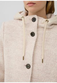 Veste en polaire rose clair avec une capuche, présentant une surface texturée, des boutons noirs et des cordons beiges avec des accents métalliques.