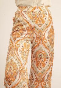 Pantalons larges à motifs ornés de fleurs orange et vertes sur un fond clair. Fabriqués dans un tissu lisse et léger.