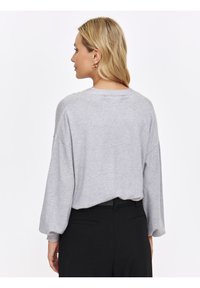 Jasnoszary sweter o luźnym kroju, z opuszczonymi ramionami i długimi rękawami. Miękka tekstura, okrągły dekolt i skrócony krój.