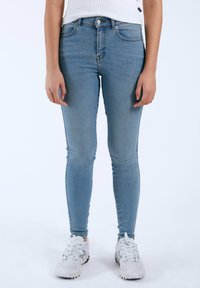 Jeans ajustados de tiro alto en azul claro con una textura suave y un ligero desvanecimiento; combinados con zapatillas deportivas blancas.