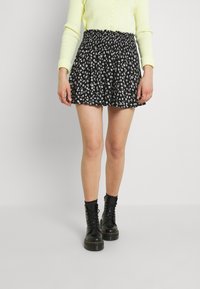 Gonna nera con stampa floreale, con vita arricciata, di lunghezza corta e tessuto fluido. Abbinata a stivali combat neri e a un cardigan giallo chiaro.
