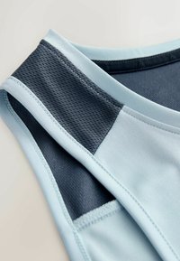 Gros plan sur un haut de sport sans manches bleu clair et gris foncé avec des panneaux en tissu maille et des coutures surpiquées.