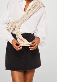 Camisa blanca de manga larga con mangas abullonadas, combinada con una falda de mezclilla negra. Una bufanda de punto beige está enrollada alrededor del torso.