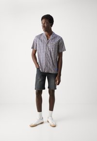 Camisa de manga corta con un patrón geométrico en azul y blanco, combinada con pantalones cortos de mezclilla oscura y zapatillas blancas. Tejido suave, ajuste relajado.