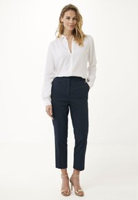 Bílá košile s dlouhými rukávy, doplněná námořnickými kalhotami na míru a zlatými vysokými podpatky. Jednoduchý a klasický design outfitu.