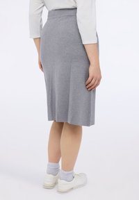 Harmaa polvipituinen hame, joka on valmistettu pehmeästä kankaasta, jossa on sileä tekstuuri. Hameessa on istuva vyötärö ja hienovaraisia laskoksia takana.