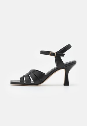 Schwarze Leder-High-Heelsandale mit Riemchen, einem Knöchelriemen und einer goldenen Schnalle, quadrater Zehenform und schlankem, skulptiertem Absatz.