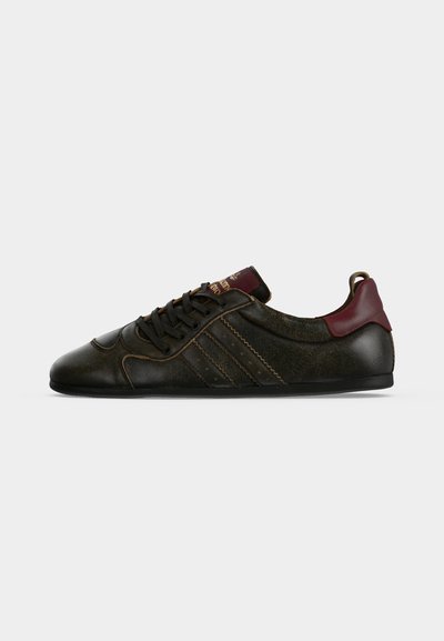 Μαύρο χαμηλό sneaker με σκούρο κόκκινο ταμπελάκι στη φτέρνα, ραμμένες πλευρικές ρίγες και μαύρα κορδόνια, εμφανίζεται από το πλάι σε γκρι φόντο.
