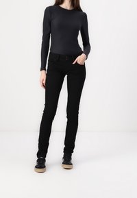 Svart långärmad topp kombinerad med svarta slim fit jeans, som har en mjuk textur. Skorna är svarta med en ljus sula.