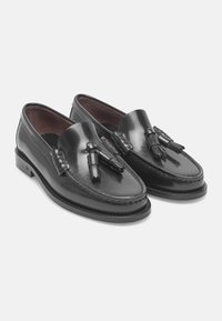 Mocassins en cuir noir avec des accents de frange, finition lisse, détails cousus et une doublure en cuir marron sur une semelle plate.