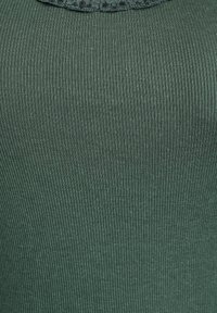 Grünes, geripptes Tanktop mit strukturierter Stoffoberfläche, rundem Ausschnitt und dezentem Glanz. Das Material ist weich und elastisch.