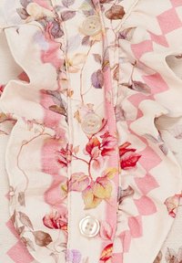 Blomstret bluse med rynkede detaljer, der har rosa og cremefarver, knaplukninger og et tekstureret stof med bladmønstre.